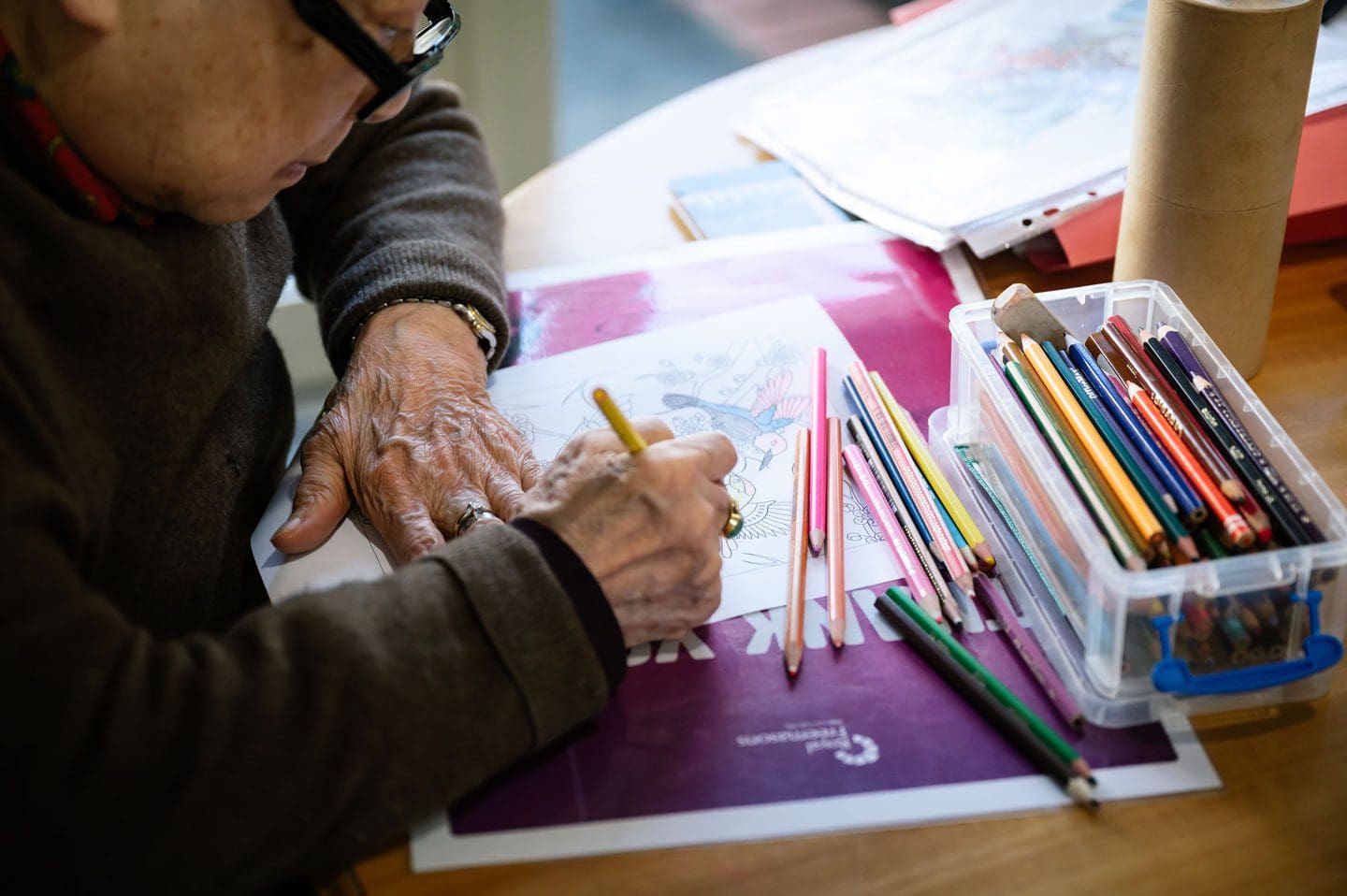 An older man is drawing at a table with colored pencils.
